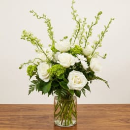 White roses and green blooms arranged in a clear glass vase