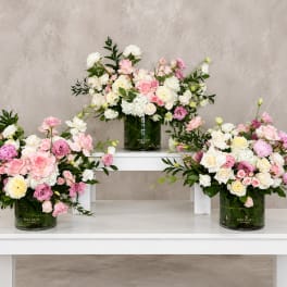 Three pastel floral arrangements in dark glass vases on white tables