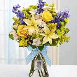 Bouquet of yellow and purple flowers in a glass vase with a blue ribbon and photo charm