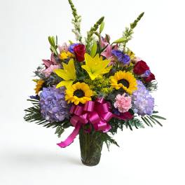 Mixed bouquet of lilies, roses, sunflowers, and hydrangeas in a glass vase