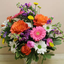Mixed bouquet of orange roses, pink gerbera daisies, and white daisies in a patterned vase
