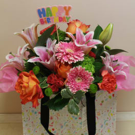 Birthday flower arrangement in a gift bag with pink lilies and roses