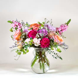 Mixed pink, purple, and orange flowers in a clear glass vase