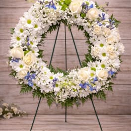 White floral wreath with cream roses and blue accents on a stand