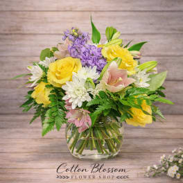 Bouquet of yellow roses, purple blooms, and white daisies in a glass vase