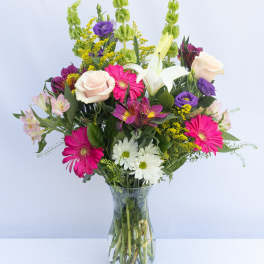 Mixed bouquet of pink, white, purple, and yellow flowers in a glass vase