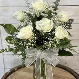 White roses in a glass vase with baby's breath and a silver ribbon