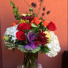 Mixed bouquet of roses, hydrangeas, and purple blooms in a glass vase