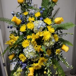 Tall floral spray with yellow roses, blue flowers, and white hydrangeas