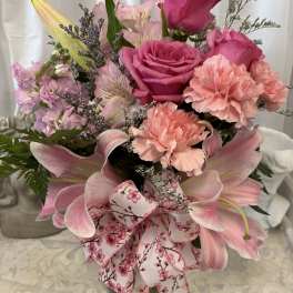 Pink roses, lilies, and carnations in a glass vase with a floral ribbon