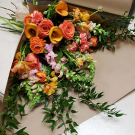 Bouquet of orange and pink flowers with trailing greenery on brown paper