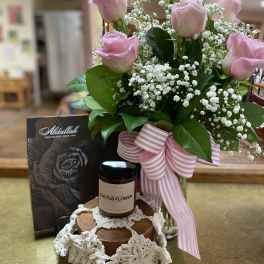 Pink roses with baby's breath in a glass vase, with chocolates and a candle