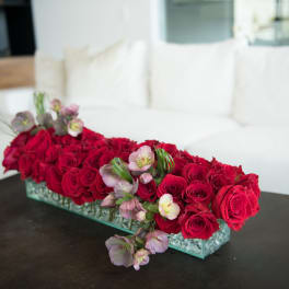 Long rectangular arrangement of red roses with pale pink flowers in a glass vase