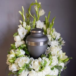 Cremation urn encircled by white roses, lilies, and carnations in a wreath-style arrangement