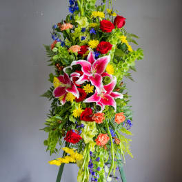Tall standing floral spray with pink lilies, red roses, and bright mixed blooms