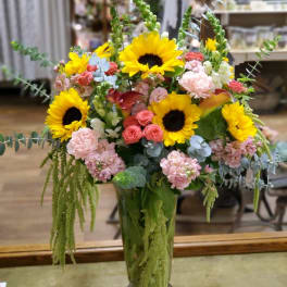 Tall mixed bouquet with sunflowers, pink blooms, and a glass vase