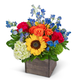 Bright mixed bouquet in a square wooden box with sunflowers, roses, and blue flowers