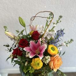 Mixed bouquet with red roses, pink lily, and yellow ranunculus in a basket