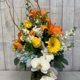 Orange lilies, yellow roses, and white orchids in a glass vase