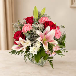 Bouquet of red roses, pink carnations, and lilies in a glass vase