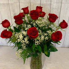 Red roses arranged in a clear glass vase with white filler flowers
