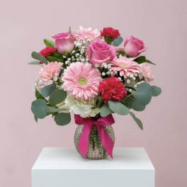 Pink roses and gerbera daisies in a glass vase with a ribbon