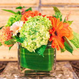Orange and green floral arrangement in a square glass vase