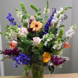 Tall mixed bouquet in a clear glass vase with pink, white, purple, and orange blooms