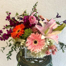 Mixed bouquet with pink lilies, gerbera daisies, and purple blooms in a glass vase