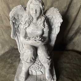Gray stone angel statue seated with wings and a small bowl in her lap