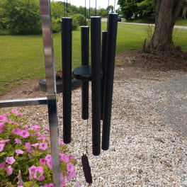 Black hanging wind chime beside pink flowers outdoors