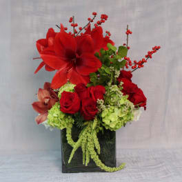Red amaryllis and roses in a black vase with green hydrangeas