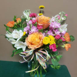 Mixed bouquet of orange, pink, white, and yellow flowers in a glass vase
