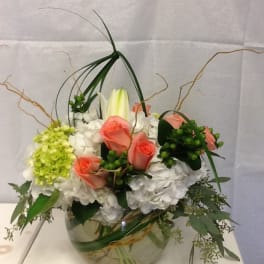 Arrangement of pink roses, white hydrangeas, and a lily in a glass bowl