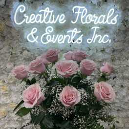 Pink roses arranged in front of a white floral wall with a glowing sign.