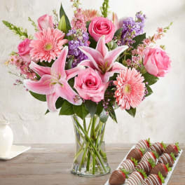 Pink bouquet in a glass vase beside a tray of chocolate-covered strawberries