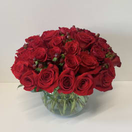 Low round arrangement of red roses with berries in a clear glass bowl vase
