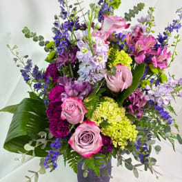 Mixed bouquet of pink roses, purple blooms, and green hydrangeas in a vase