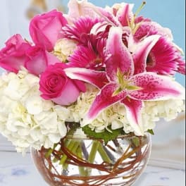 Pink roses and lilies arranged with white hydrangeas in a glass vase