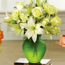 White lilies and pale yellow roses in a green glass vase