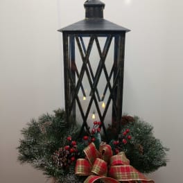 Black lantern centerpiece with candles, pine wreath, berries, and plaid ribbon
