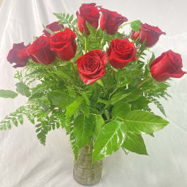 Red roses arranged in a clear glass vase with green foliage