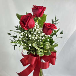 Three red roses in a glass vase with a large red ribbon