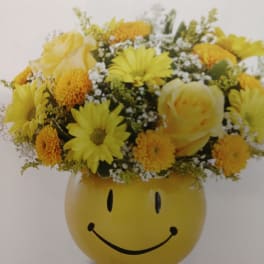 Yellow flower arrangement in a smiley-face container
