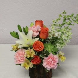 Mixed bouquet with orange roses, pink carnations, white lilies, and white filler flowers in a wood container
