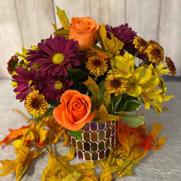 Orange roses and purple daisies in a patterned vase with autumn leaves