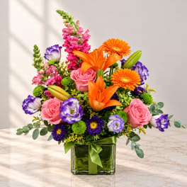 Colorful bouquet with orange lilies, pink roses, and purple blooms in a glass vase