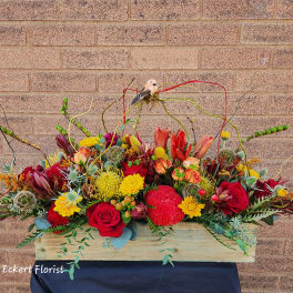 Long floral arrangement in a wooden box with red, yellow, and peach blooms