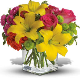 Bouquet of yellow lilies, pink roses, and purple mums in a clear glass vase