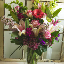 Mixed bouquet of lilies, roses, and purple flowers in a glass vase